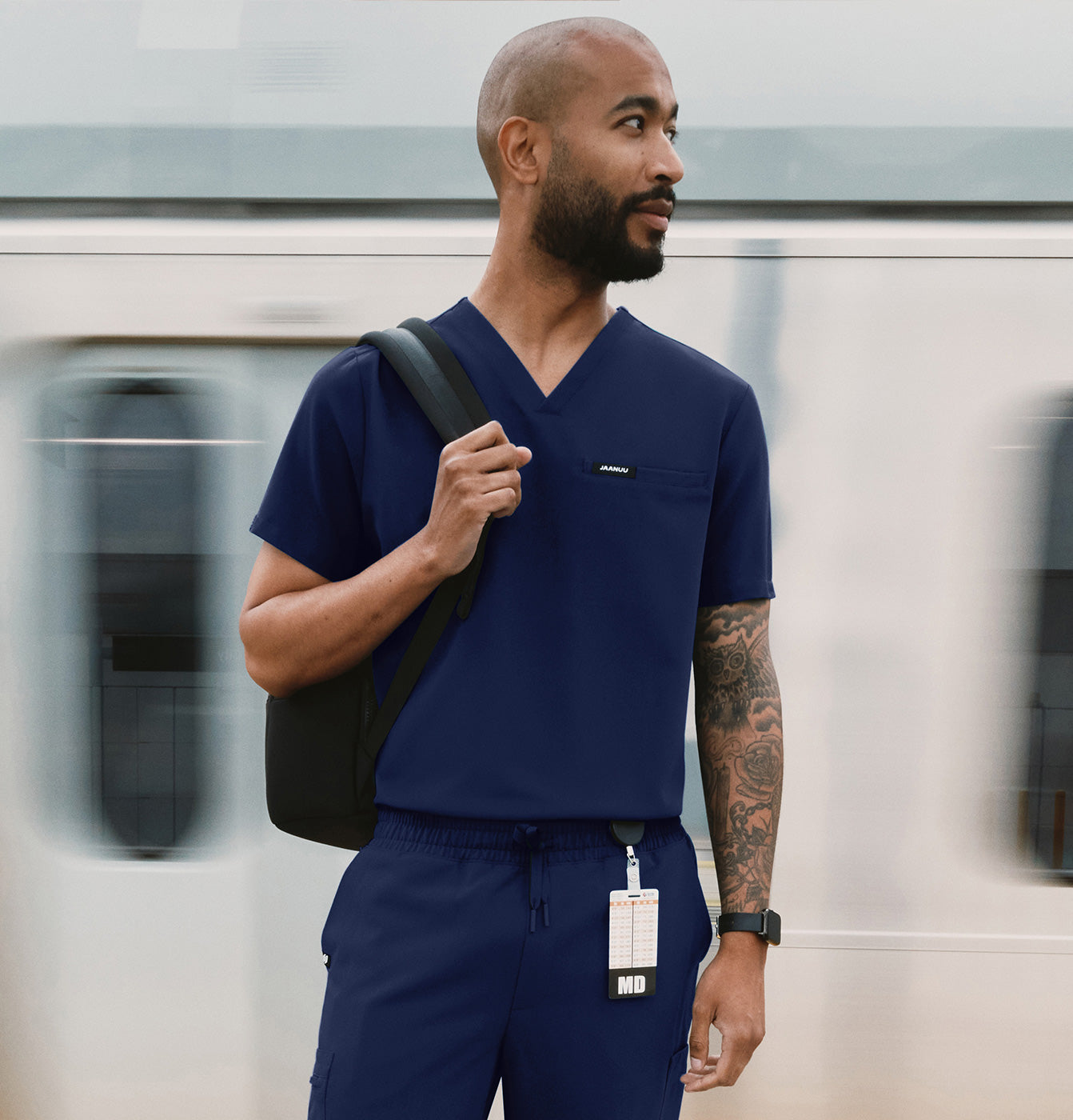 A man wearing scrubs with a backback standing by a train.