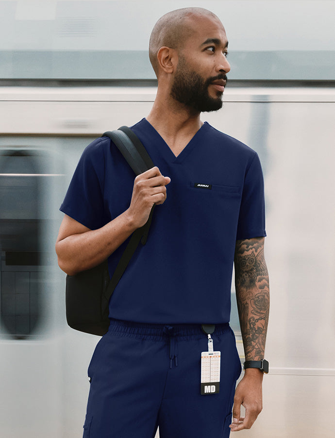 A man wearing scrubs with a backback standing by a train.