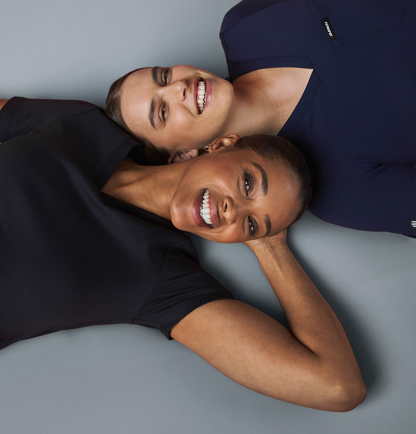 Two women wearing scrubs smiling.