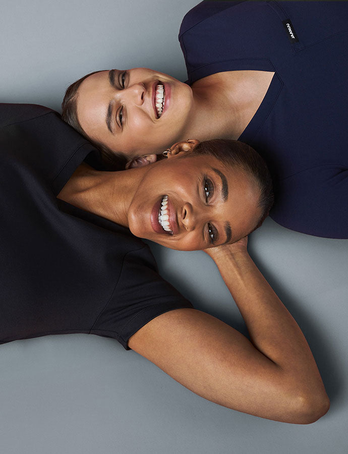 Two women wearing scrubs smiling.