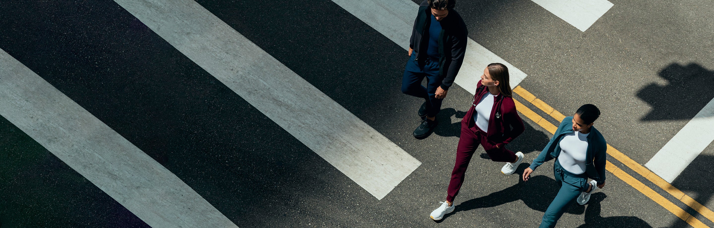 A man and two women wearing underscrubs, jackets, and scrub pants walking across the street.