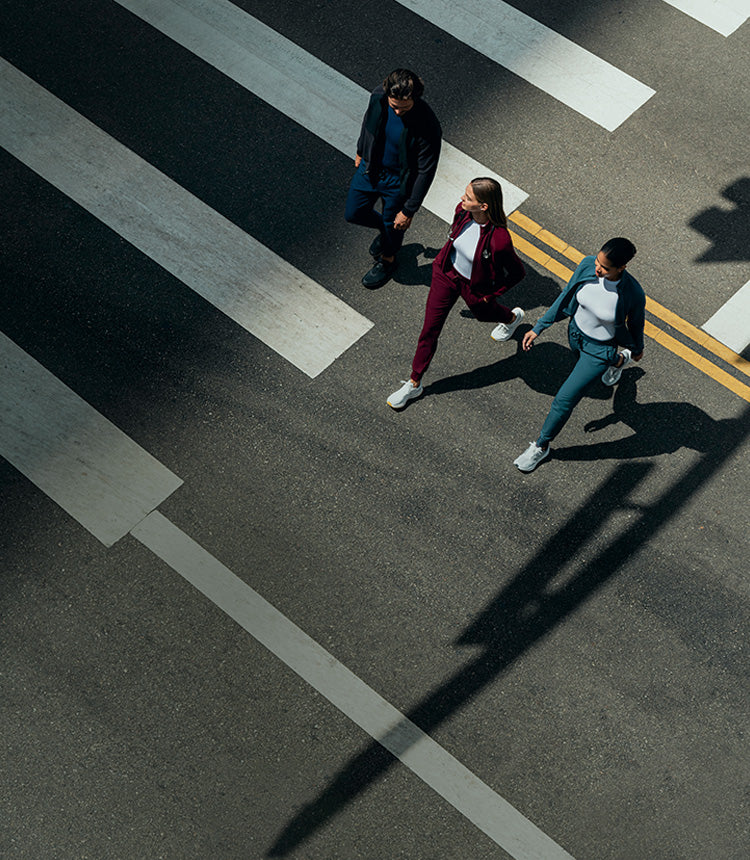 A man and two women wearing underscrubs, jackets, and scrub pants walking across the street.